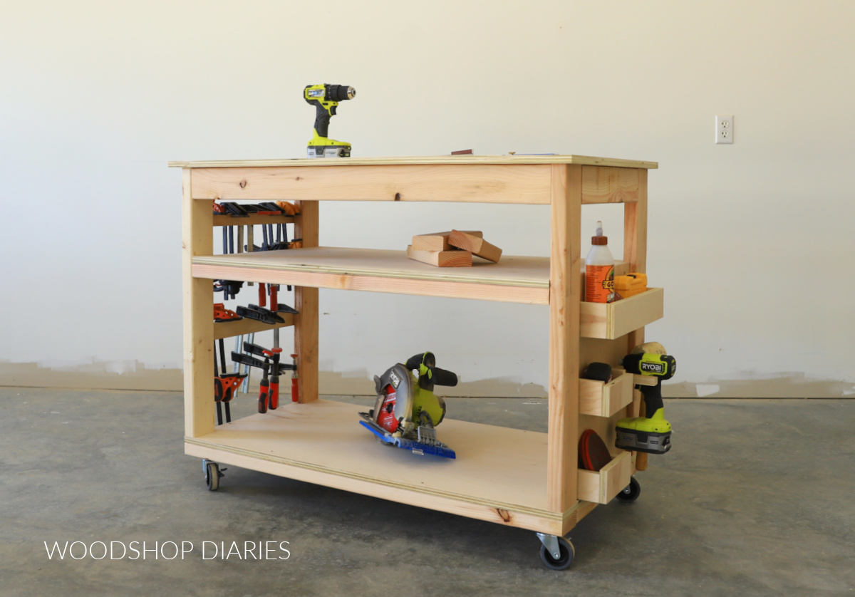 Mobile small space workbench with tool storage installed on one side and clamp storage on the other. A circular saw sitting on the bottom shelf and scrap blocks on the middle shelf.