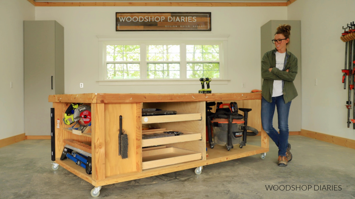 Shara Woodshop Diaries posing next to finished workbench project with storage drawers in workshop