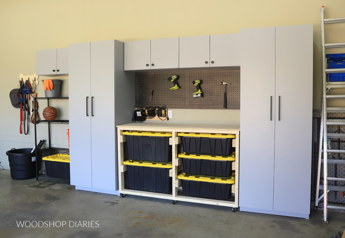 Two tall garage cabinets with workbench in the middle and upper cabinets above workbench with pegboard panel and battery charger