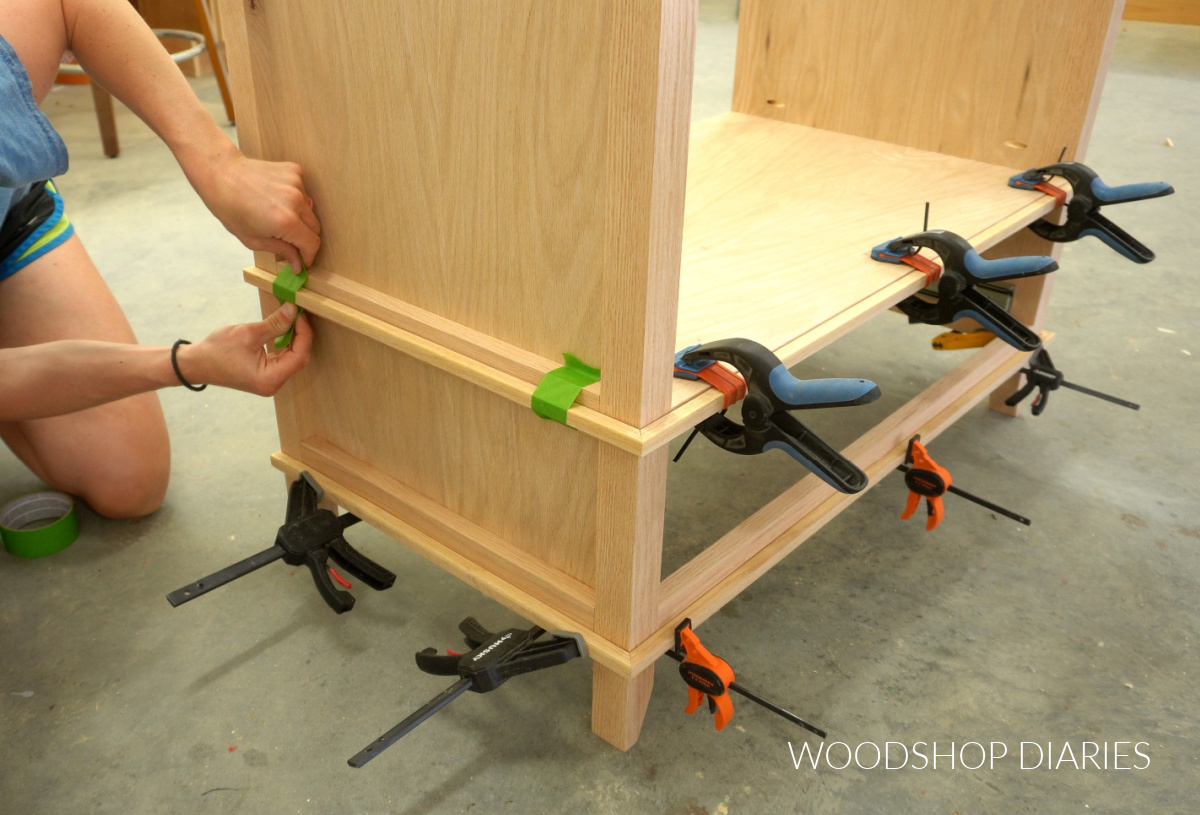 Shara Woodshop Diaries applying painters tape to hold trim pieces on vanity while glue dries