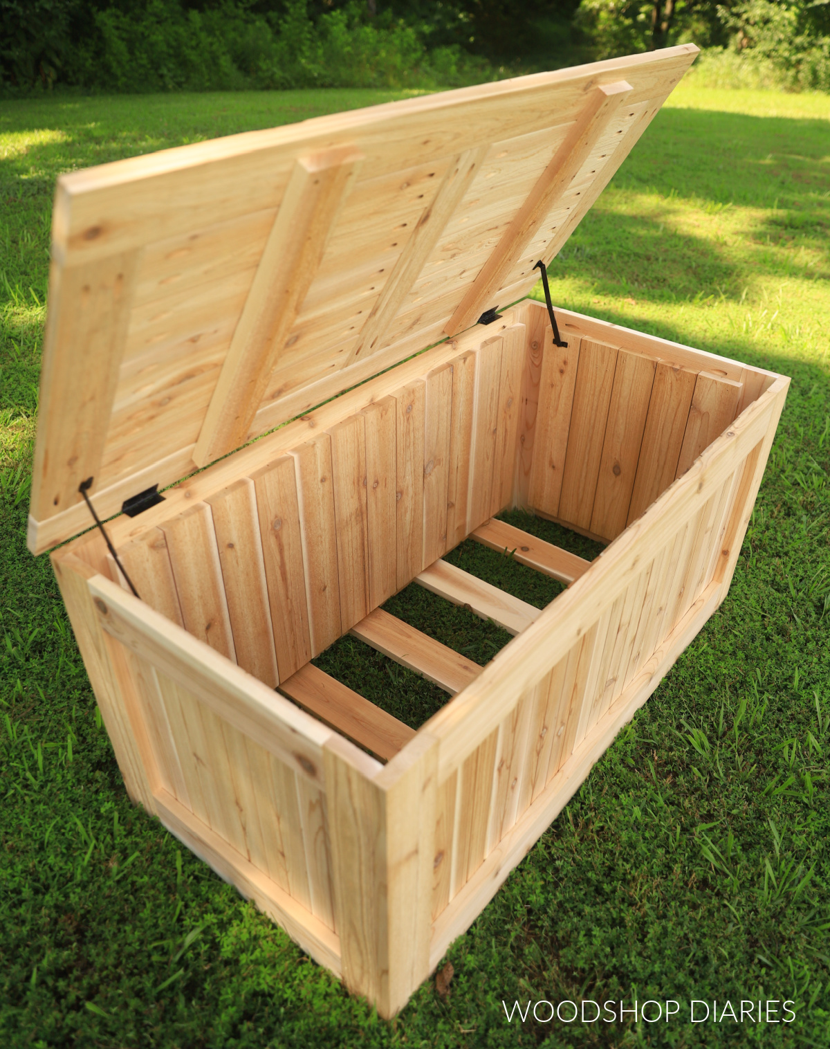 outdoor wooden storage box in yard with lid open showing bottom slats spaced out for drainage