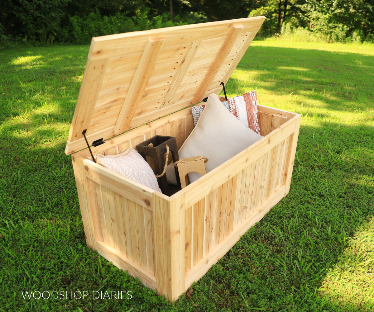 Completed DIY outdoor storage box in yard with lid open--outdoor cushions, lanterns, and decor stored inside