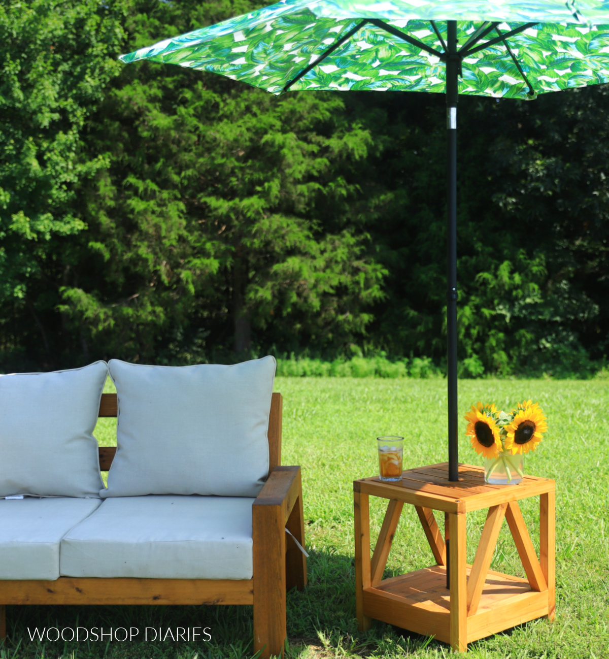 DIY wooden umbrella stand side table with palm leaf umbrella next to outdoor wooden sofa couch with cushions in grassy yard