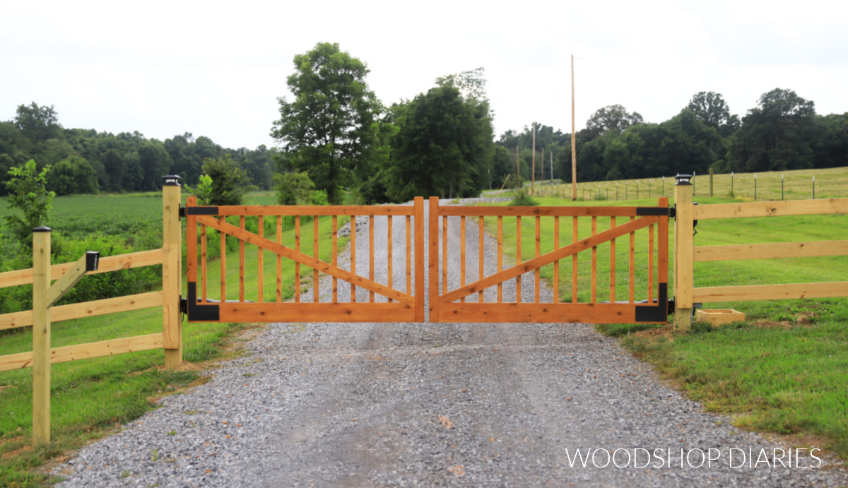 Finished DIY wooden driveway gates  installed on posts with fencing extending out both sides. Keypad for gate entry mounted on post on left side of driveway