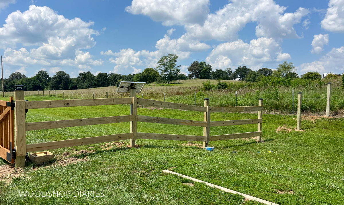 DIY wooden fence half completed extending out from driveway gates
