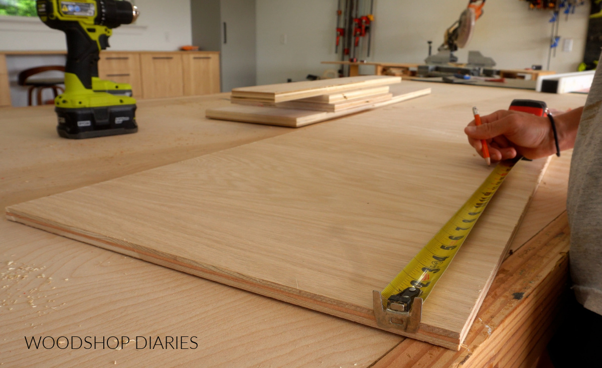 Shara Woodshop Diaries measuring and marking ½" plywood 16 ½" square on workbench