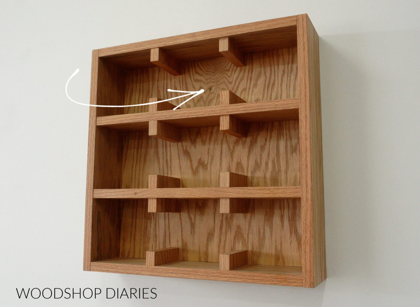 Wall mounted mug shelf with arrow pointing to screw used to secure it to wall studs through back panel