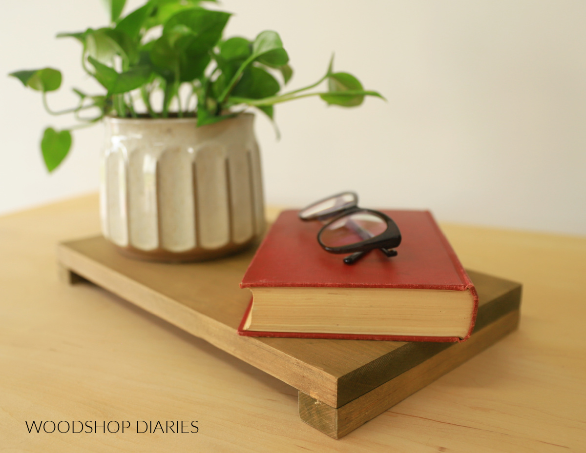 Finished pine wood riser with edge pieces glued along ends with plant and book on top