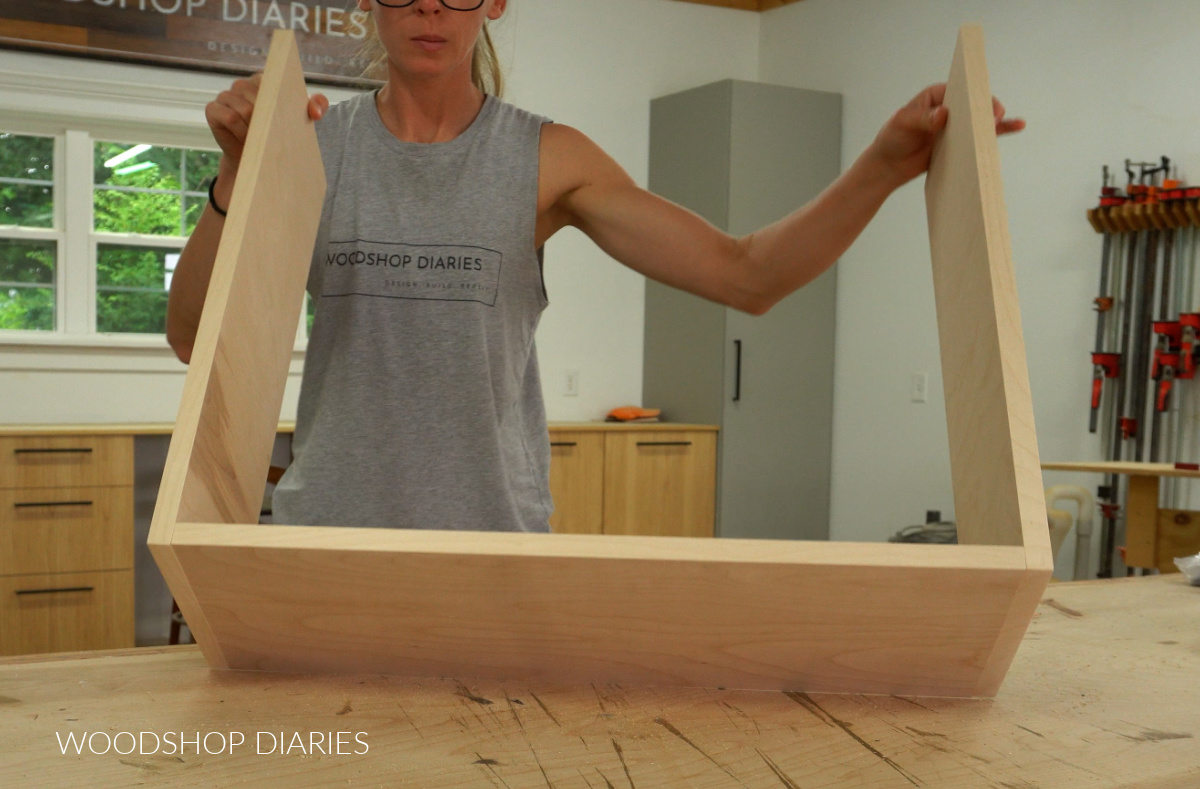 Shara Woodshop Diaries holding up assembled bottom piece of cabinet organizer pull out