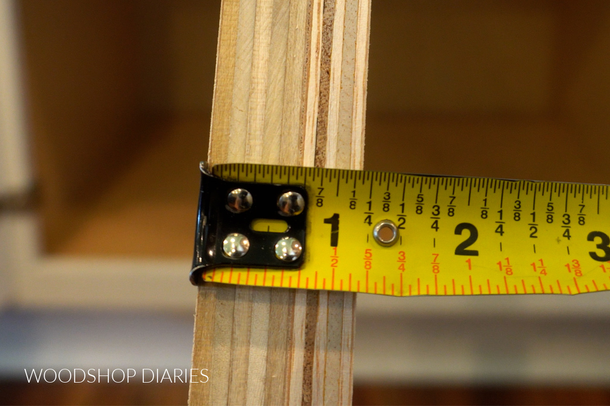 Tape measure measuring thickness of plywood spacer block for drawer slides inside cabinet