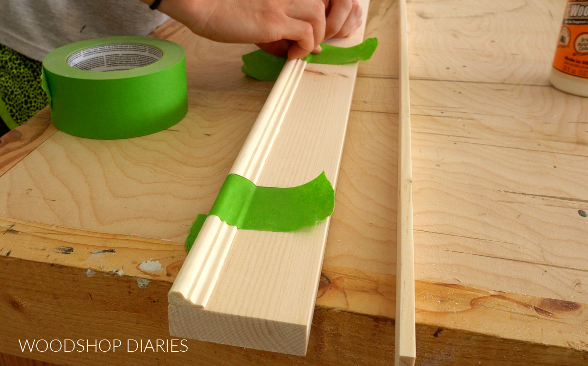 Using painters tape to secure chair rail molding to wood board for picture frame