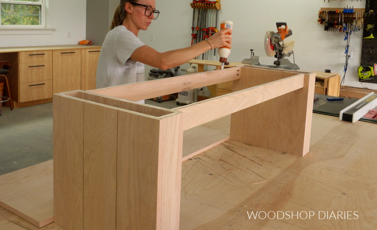 Shara Woodshop Diaries applying wood glue to top of bench base on workbench