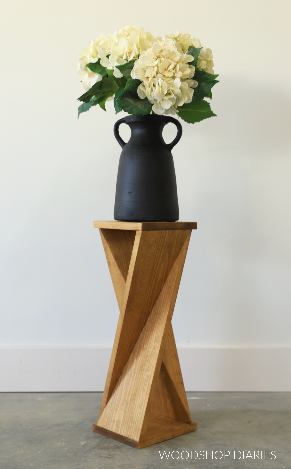 Finished DIY twisty table made from a single 1x8 board stained Minwax Early American with a flower vase on top