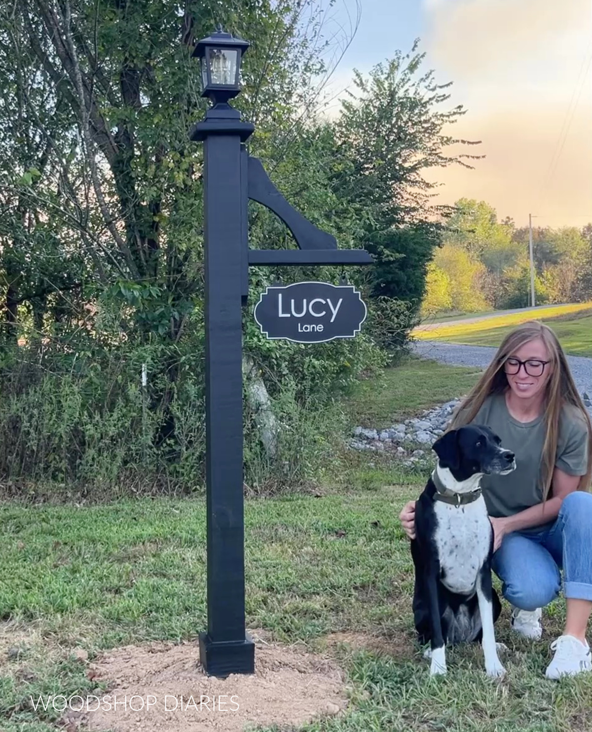 Shara Woodshop Diaries with dog Lucy sitting next to wooden lamp post with "Lucy Lane" sign