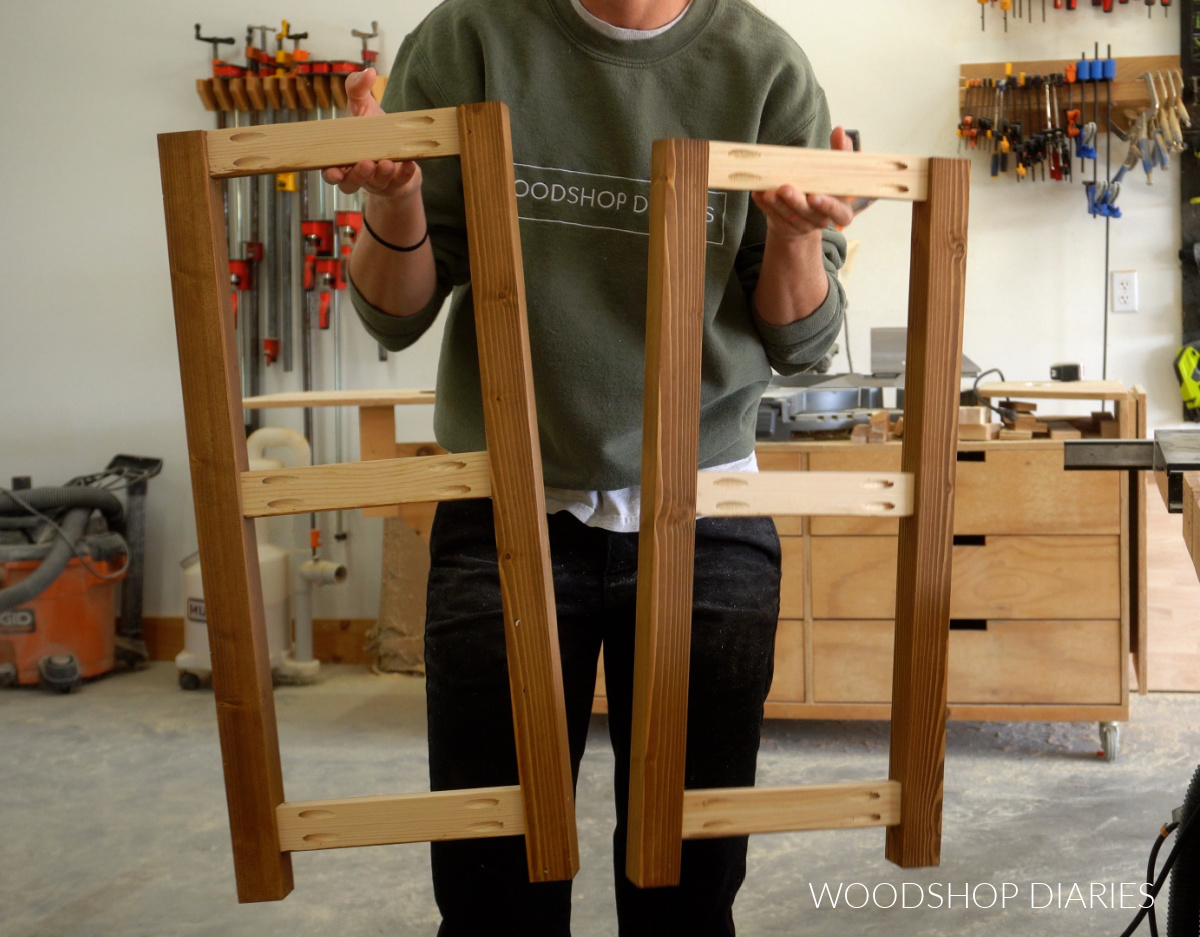 Shara Woodshop Diaries holding up side frames of console table with open shelves showing pocket hole assembly