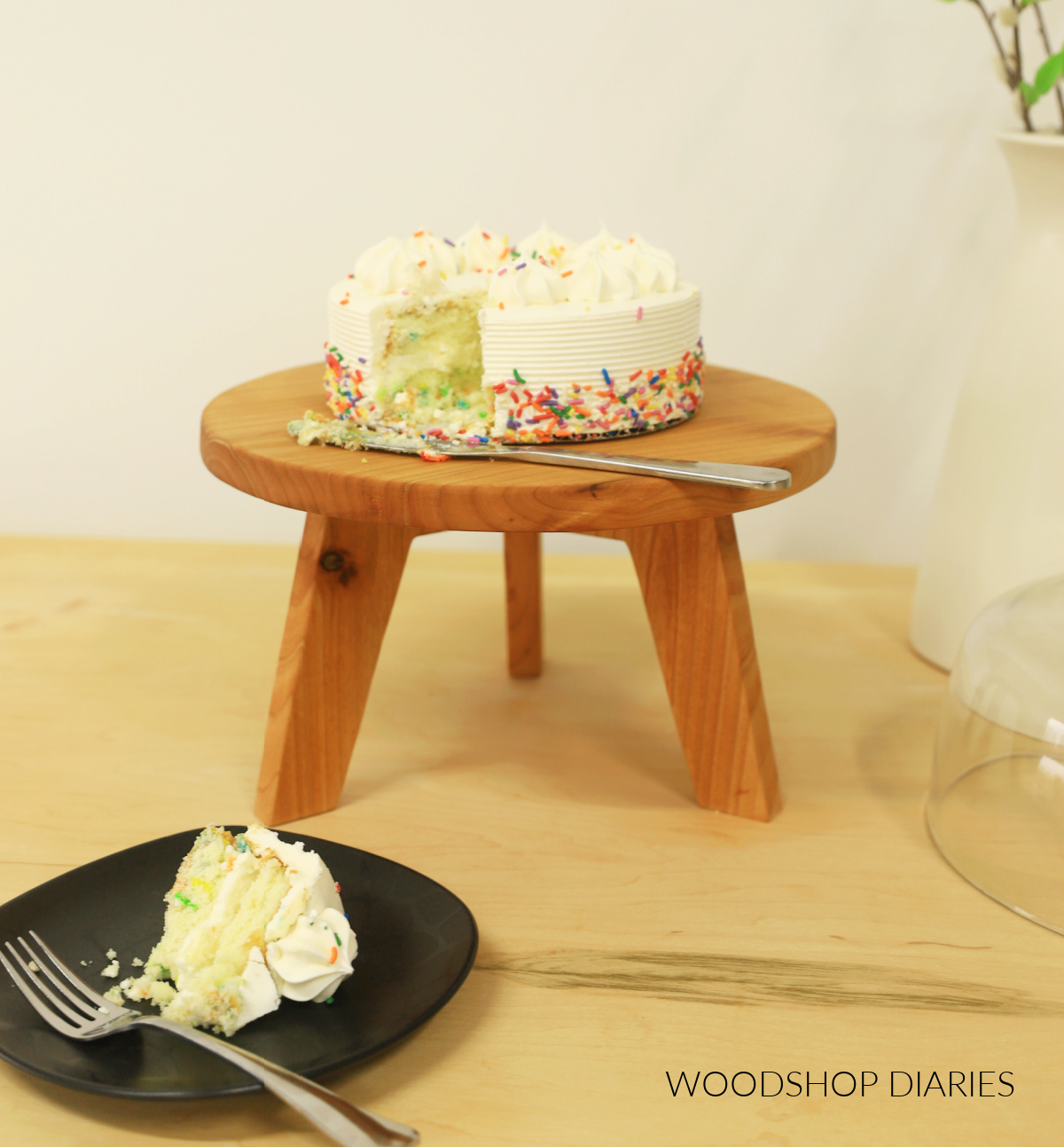 Mid century modern style wooden cake stand with birthday cake. Piece cut from cake and placed on plate