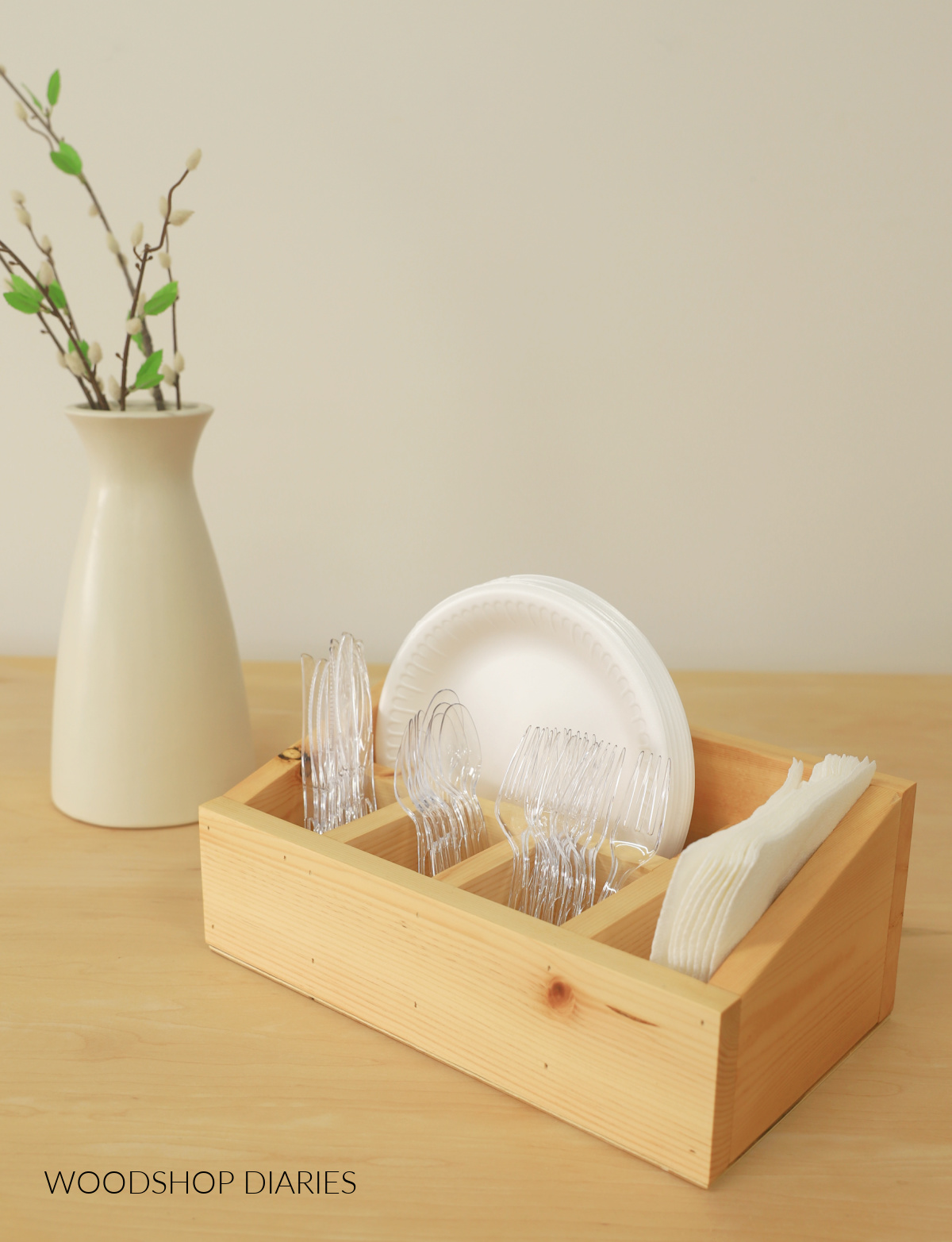 Completed DIY wooden dinnerware holder caddy full of plates, napkins, forks, spoons, and knives on tabletop