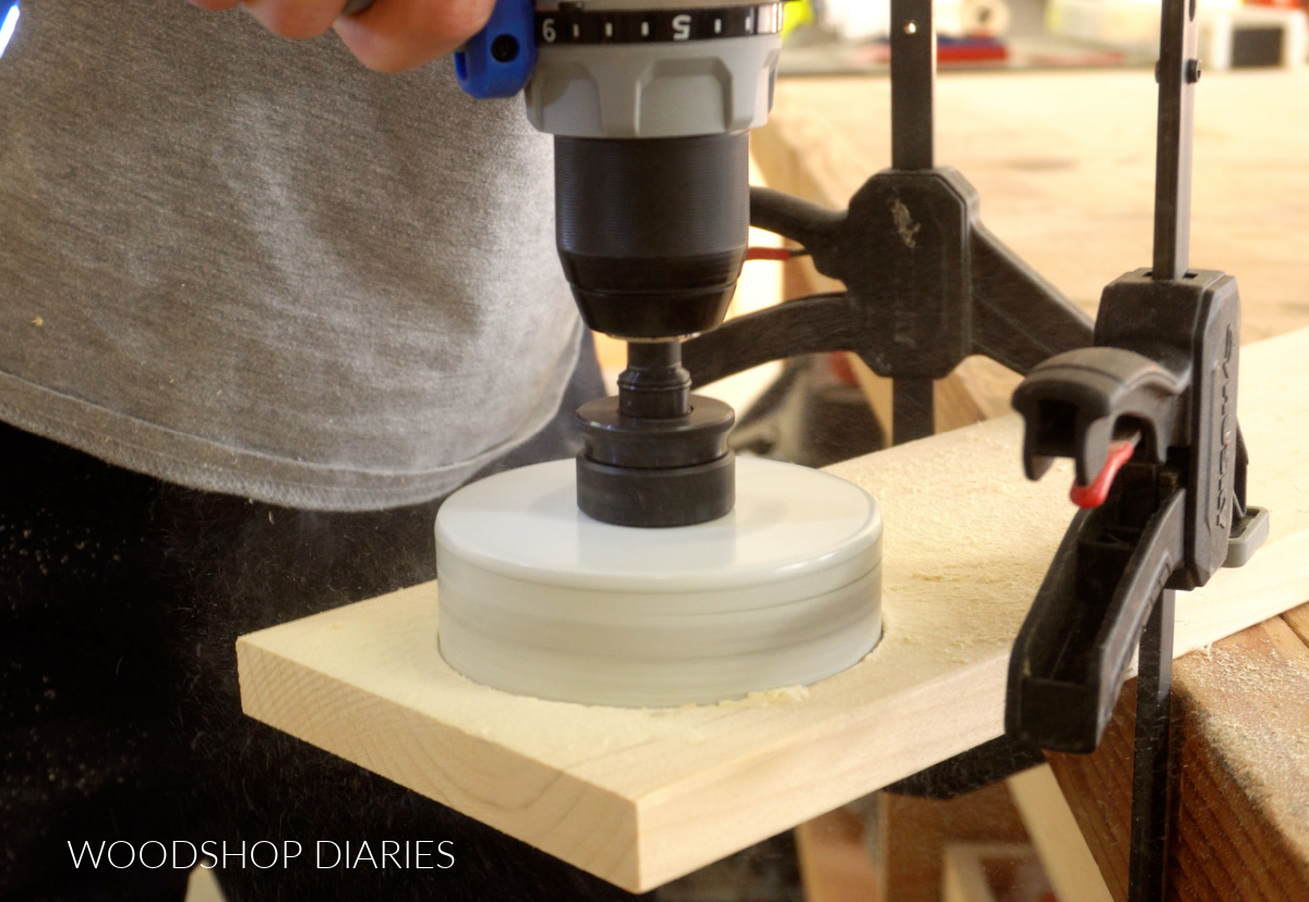 Close up of 4" hole saw drilling hole in end of 1x6 board on workbench