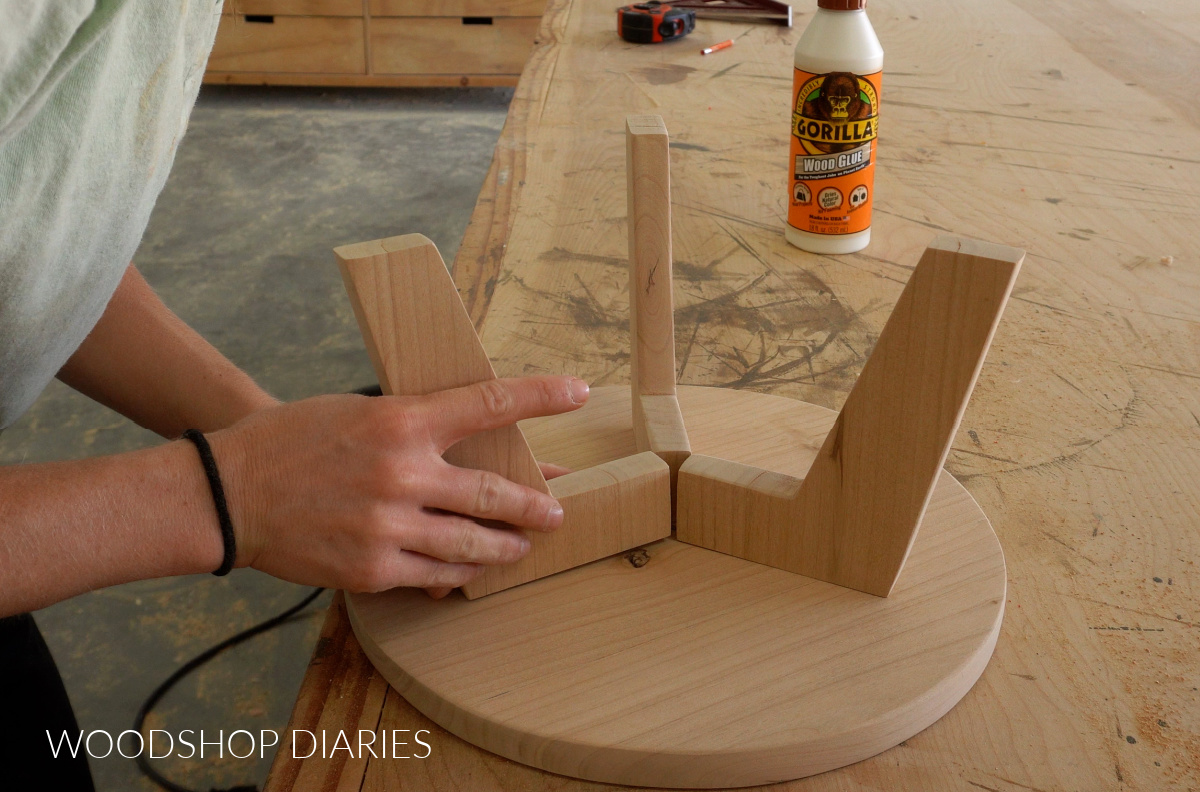 Close up of gluing mid century modern wooden legs to bottom of wooden cake stand top plate