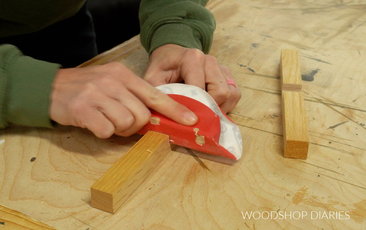 Close up of Shara Woodshop Diaries sanding notch in cross trivets on workbench