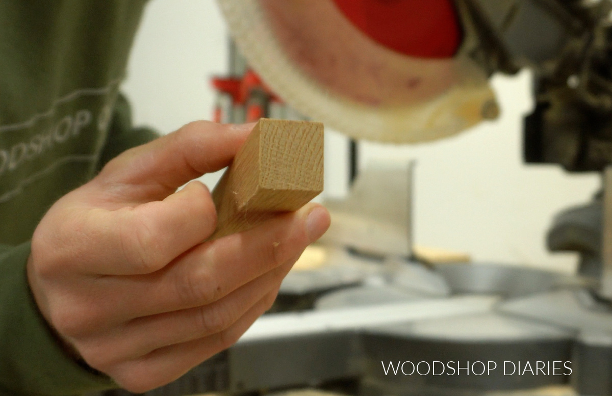 Square red oak dowel close up with miter saw in the background