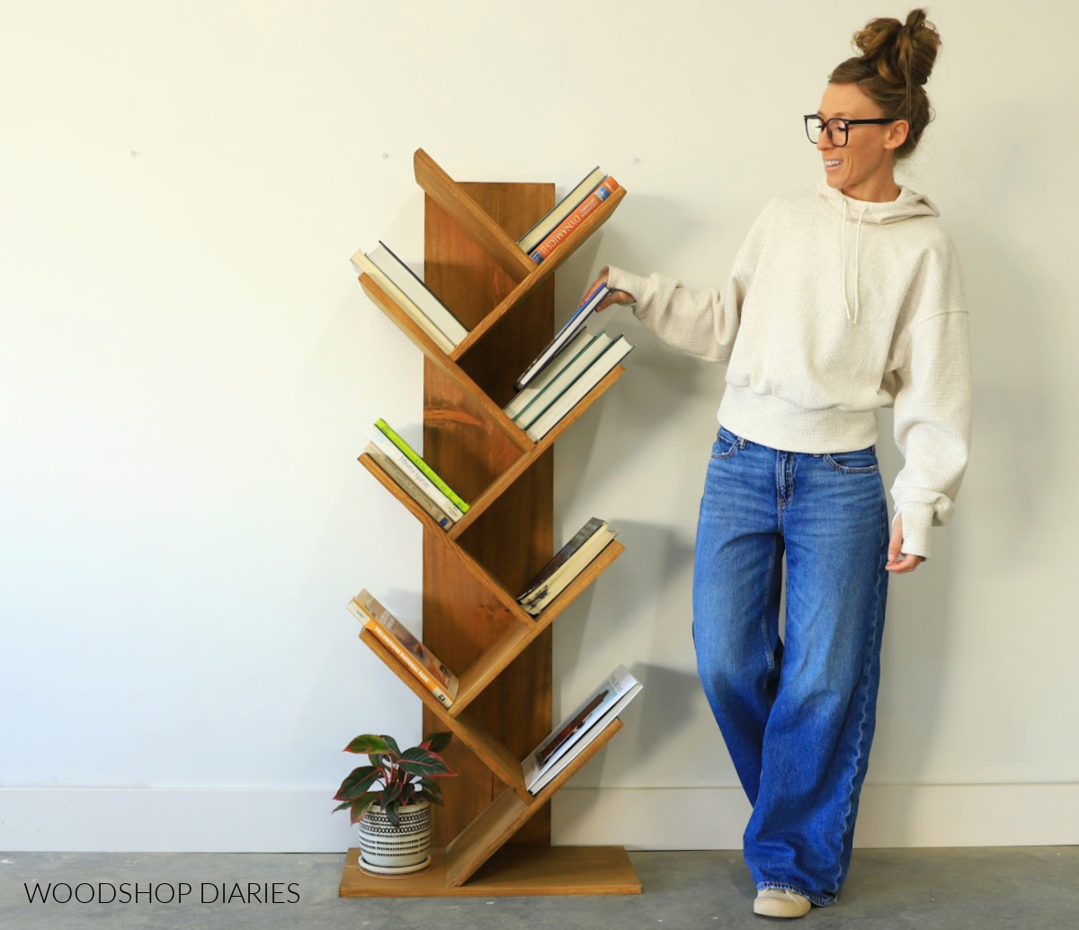 Shara Woodshop Diaries standing next to DIY angled bookshelf made from 1x12 boards