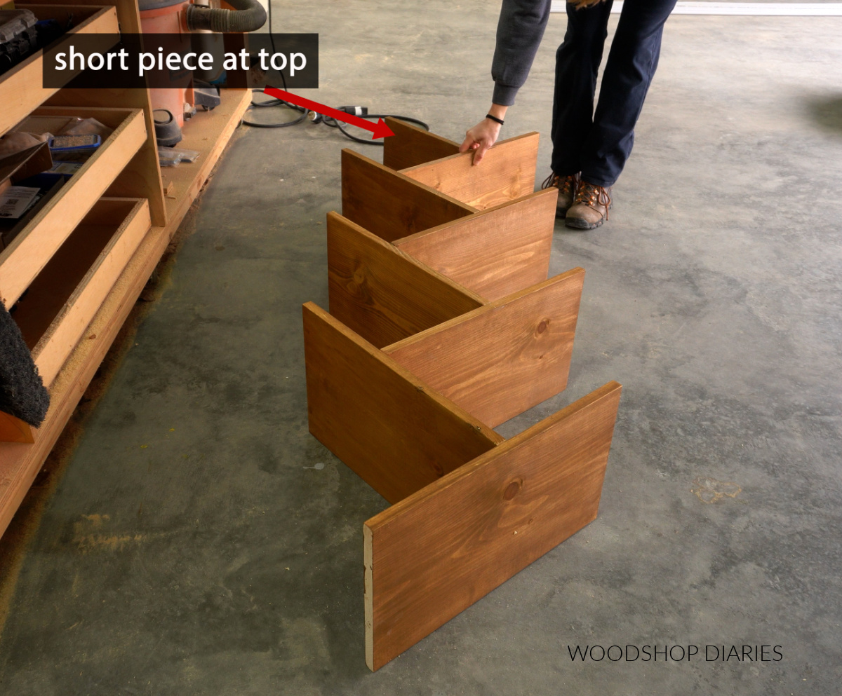 Shara Woodshop Diaries laying out "T" shaped pieces to visualize DIY angled bookshelf on workshop floor