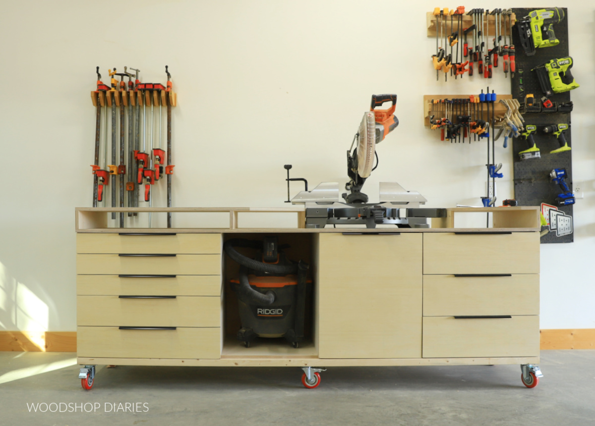Miter saw station in workshop on caster wheels with vacuum and tools in the background