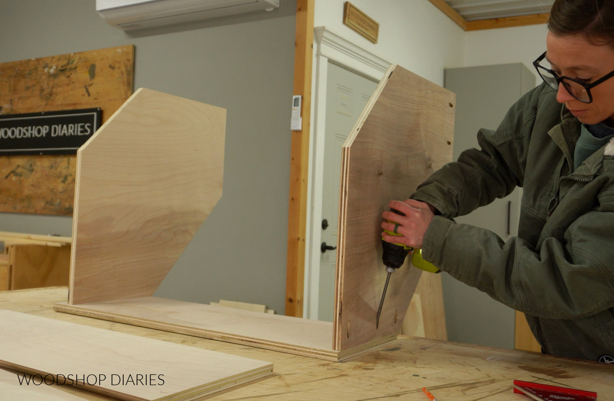 Shara Woodshop Diaries driving pocket hole screws to attach top panel to corner cabinet box