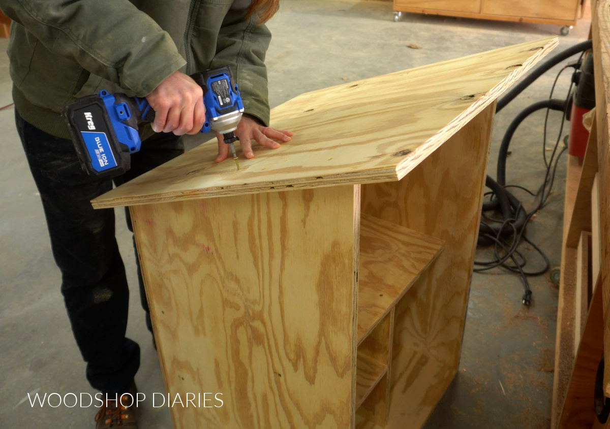 Shara Woodshop Diaries driving screws through plywood panel to secure roof to blessing box