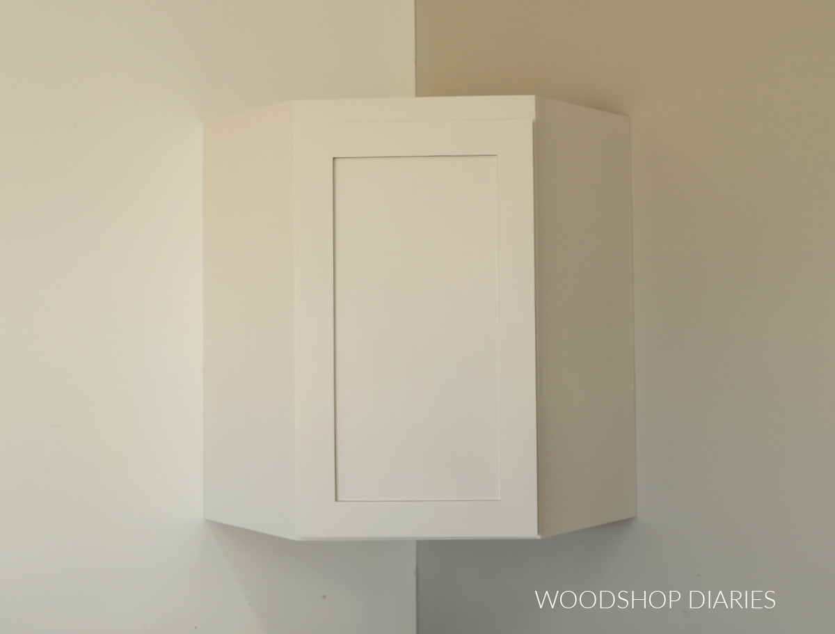 Corner wall cabinet painted grey hung on wall in corner with door closed