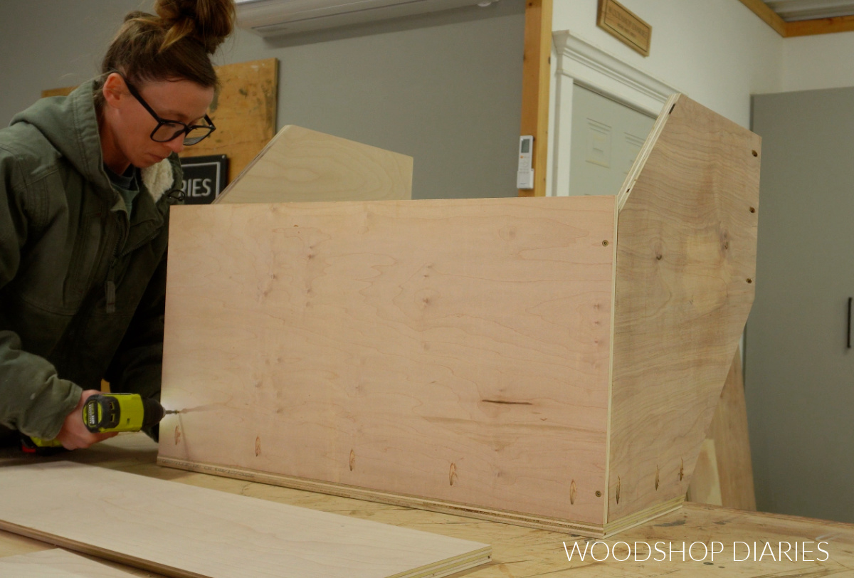 Shara Woodshop Diaries securing back panel of corner cabinet box to bottom panel on workbench