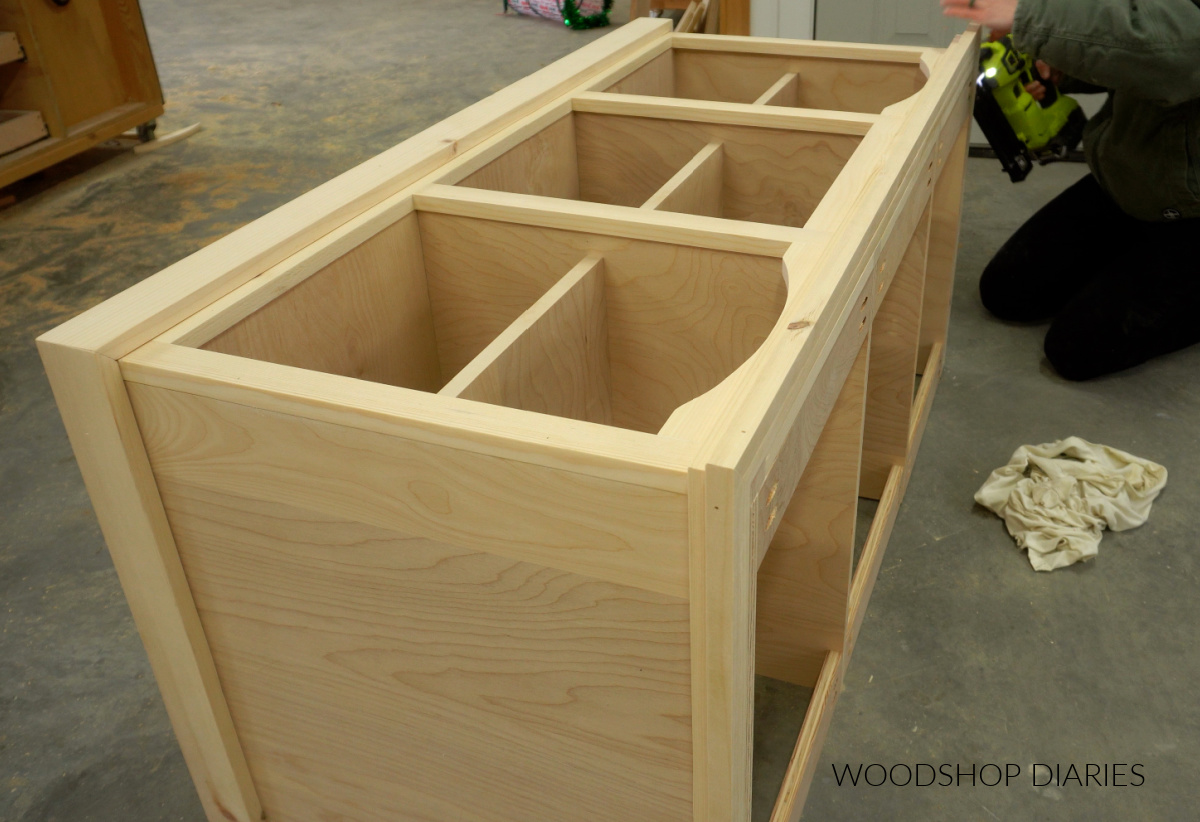 Close up of Shara Woodshop Diaries brad nailing square dowel trim around top of tv stand project