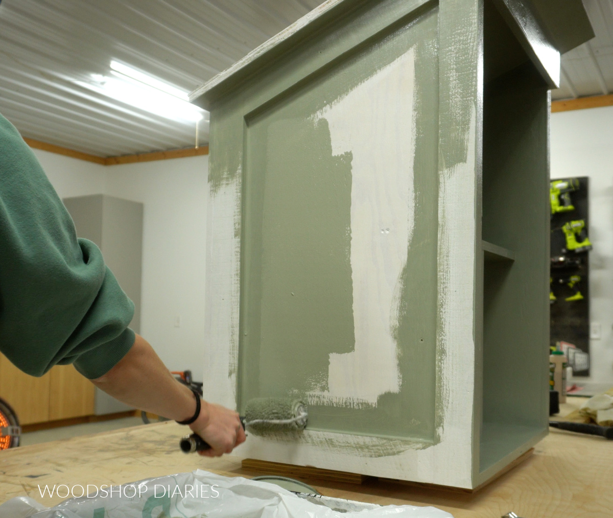 Shara Woodshop Diaries rolling paint onto side of community blessing box on workbench with paint roller