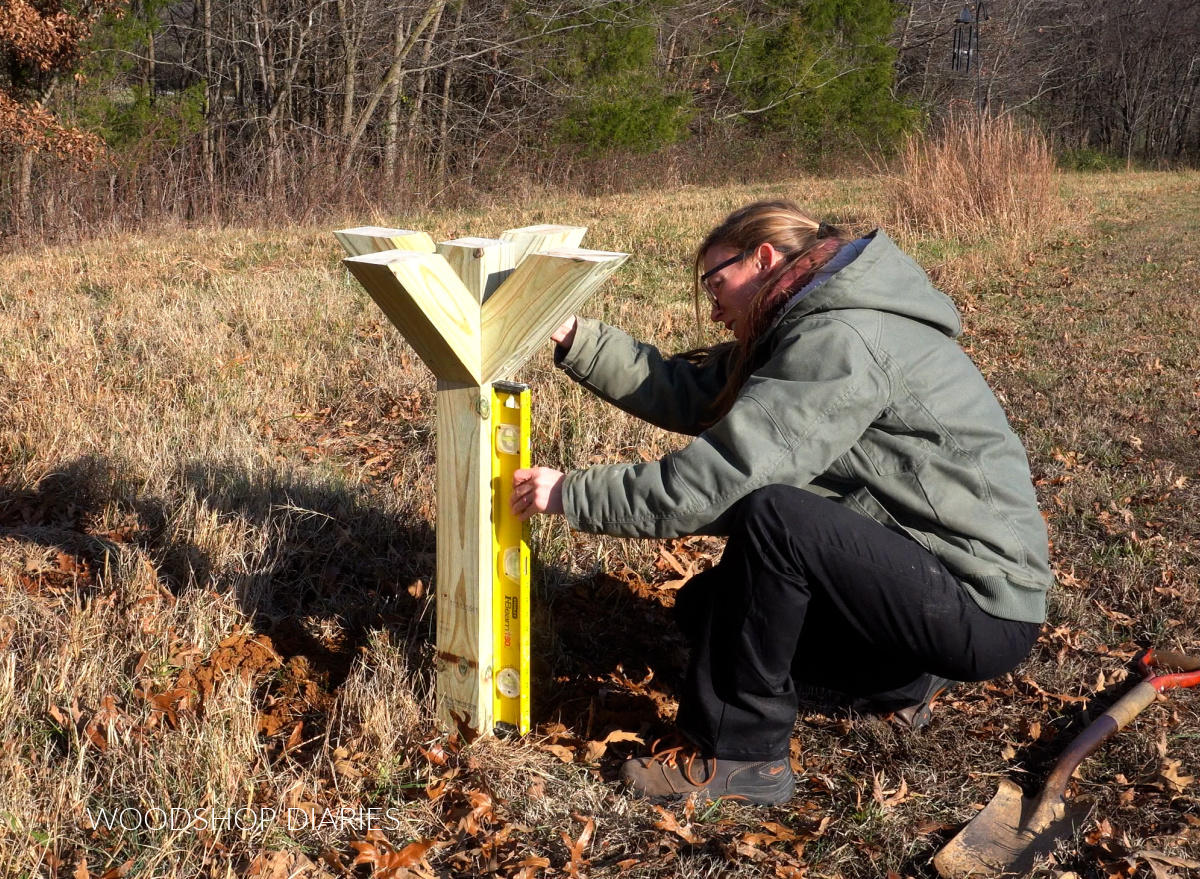 Shara Woodshop Diaries checking that post in the ground is level with a 2 ft level