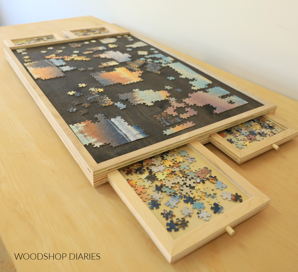 DIY puzzle board with four drawers made from scrap plywood sitting on worksurface with drawers open and puzzle pieces stored inside