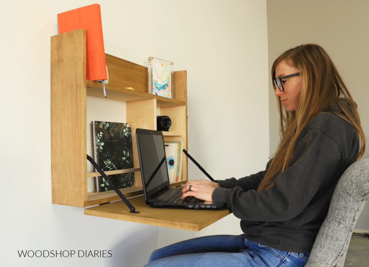 Shara Woodshop Diaries sitting at DIY Murphy Desk. Desk folded out with laptop and storage inside for books and notebooks