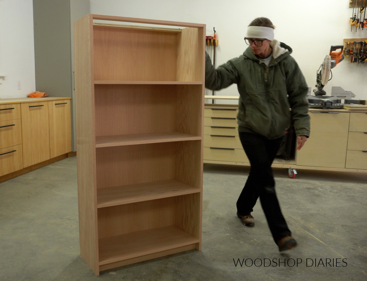 Shara Woodshop Diaries standing next to completed bookcase body with shelves and back panel added in workshop