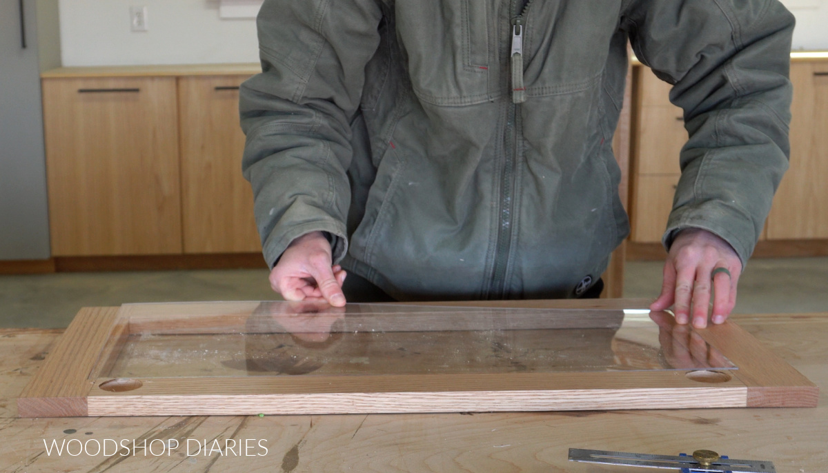 Shara Woodshop Diaries carefully placing acrylic sheet into rabbet on back side of door frame on workbench