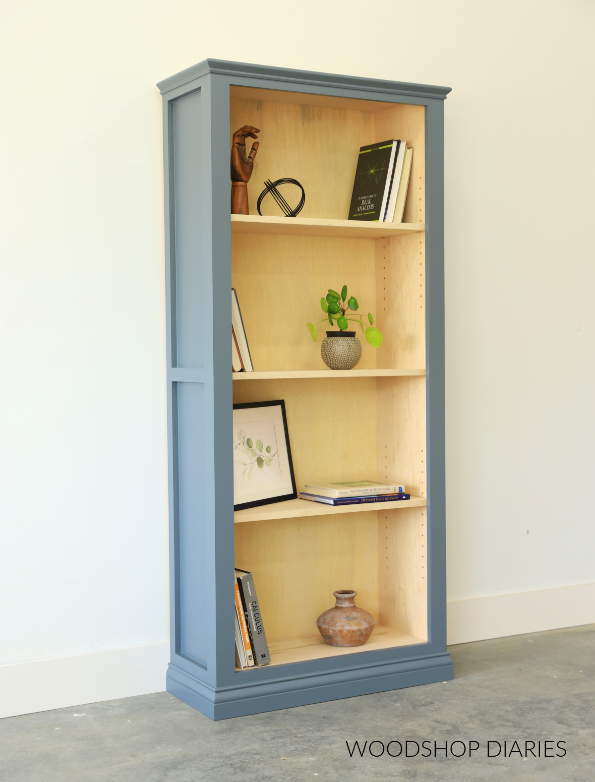 Completed DIY bookshelf with adjustable shelves painted blue with decorative baseboard and bas cap molding around top and bottom