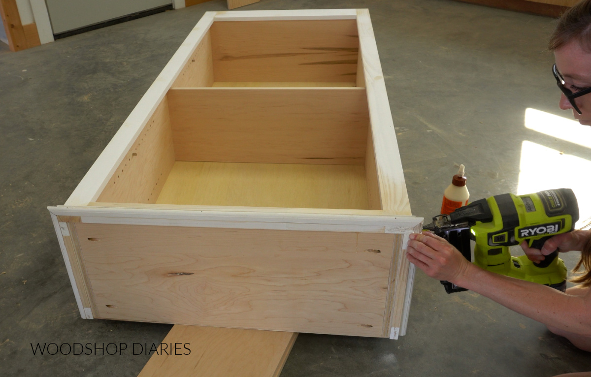 Shara Woodshop Diaries nailing decorative trim around top of bookshelf on workshop floor