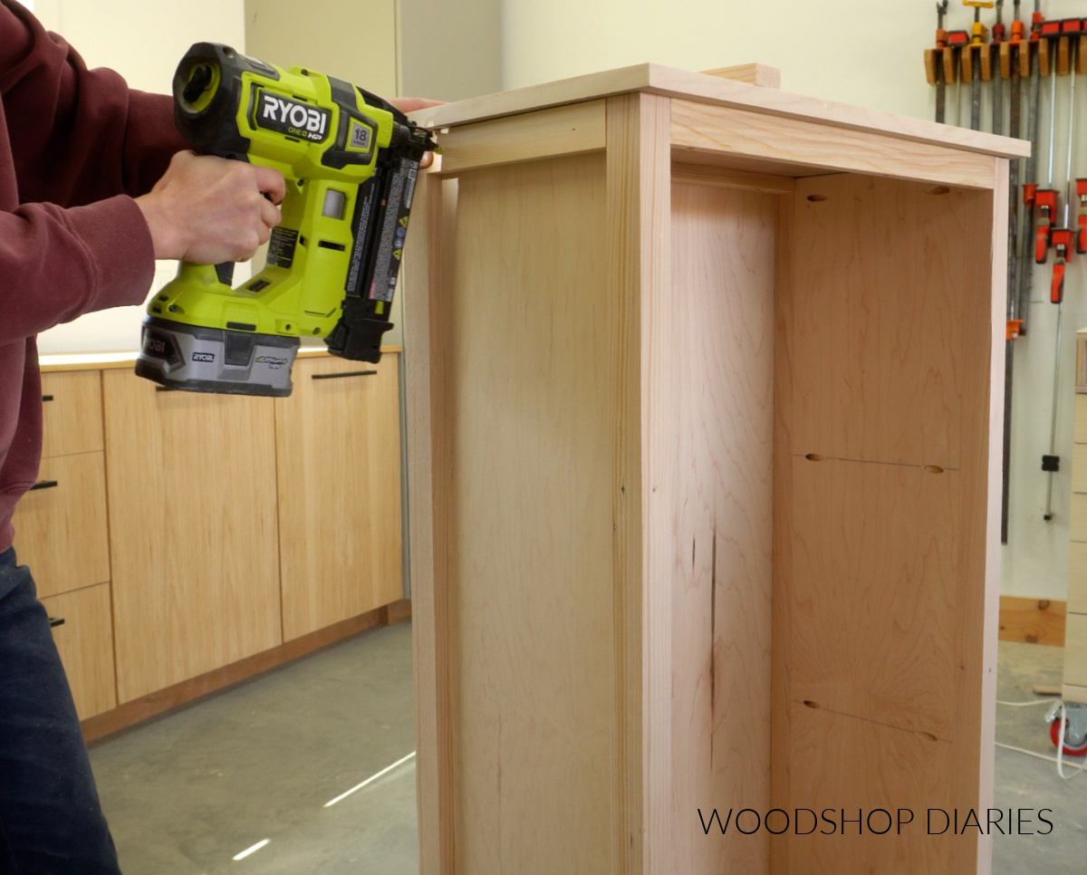 Close up of Shara Woodshop Diaries brad nailing 1x2 pieces to trim sides of bookshelf