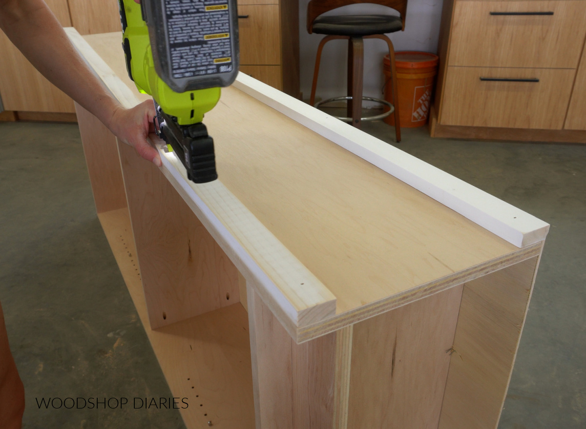 Close up of brad nailing 1x2 trim onto sides of DIY bookshelf