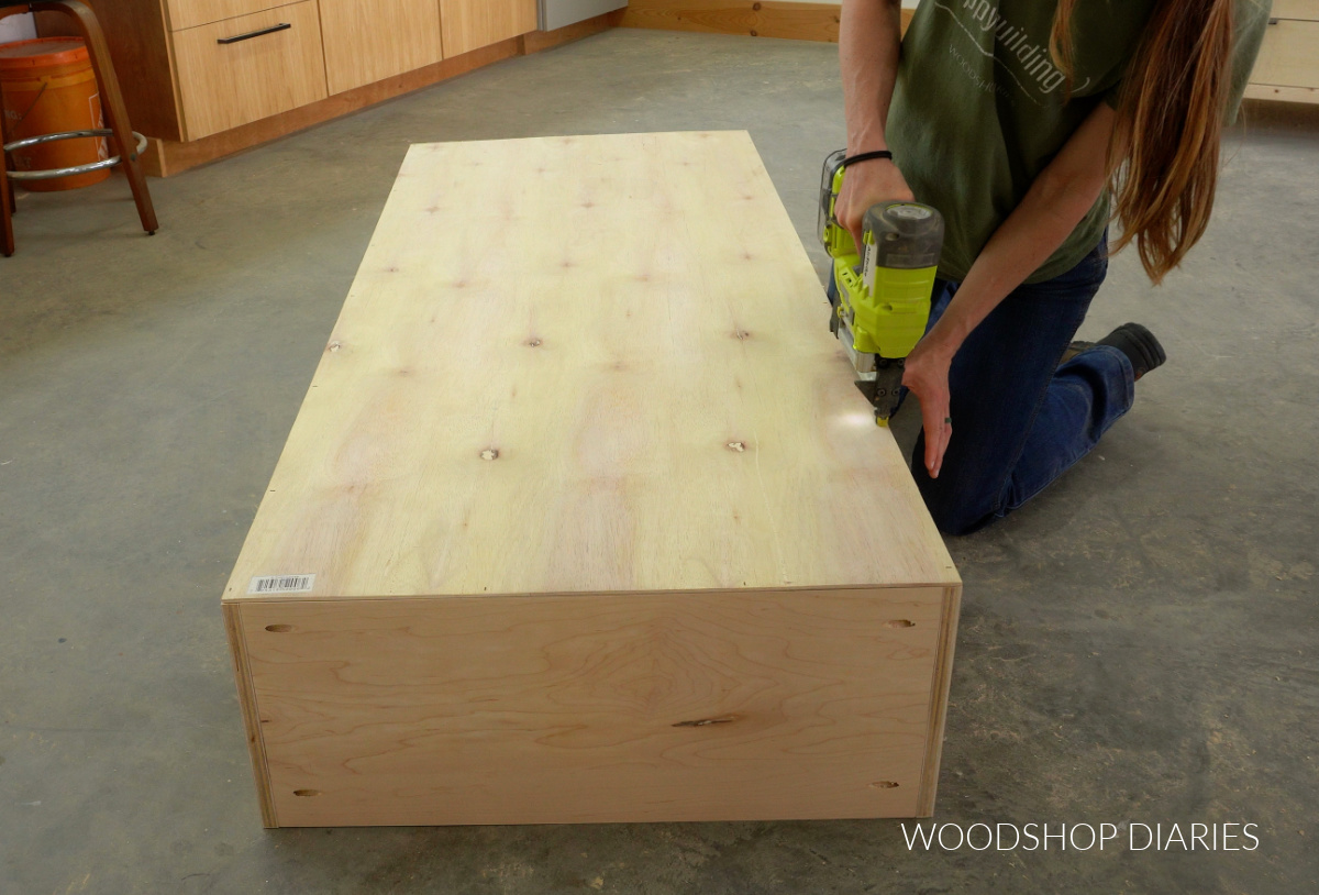 Shara Woodshop Diaries stapling back panel onto bookcase on workshop floor
