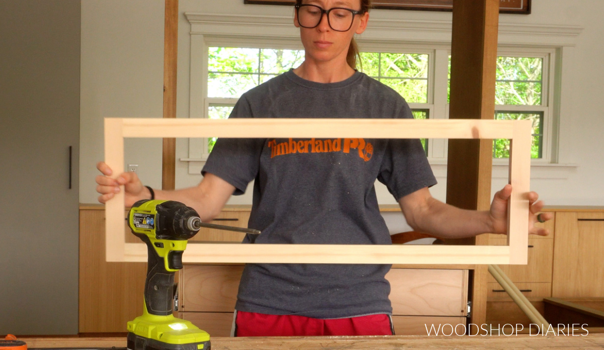 Shara Woodshop Diaries holding up 1x2 drawer front frame in workshop