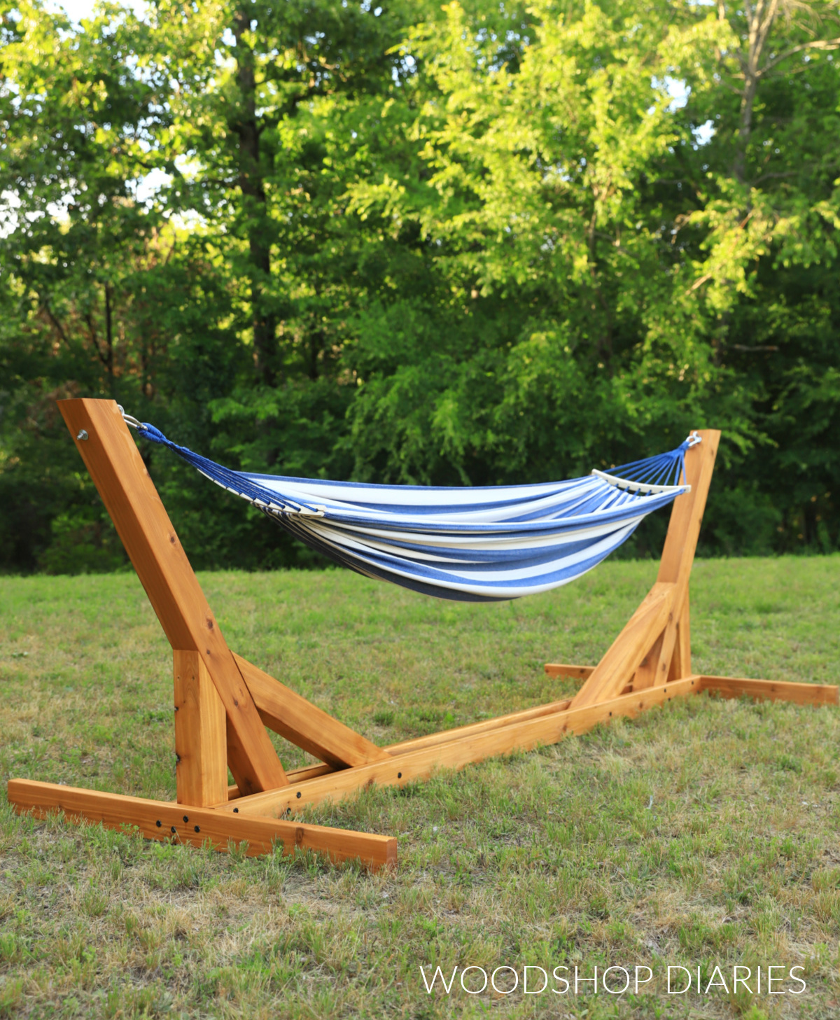 DIY hammock stand made of cedar with blue and white striped hammock hanging on it in front of trees in grass yard