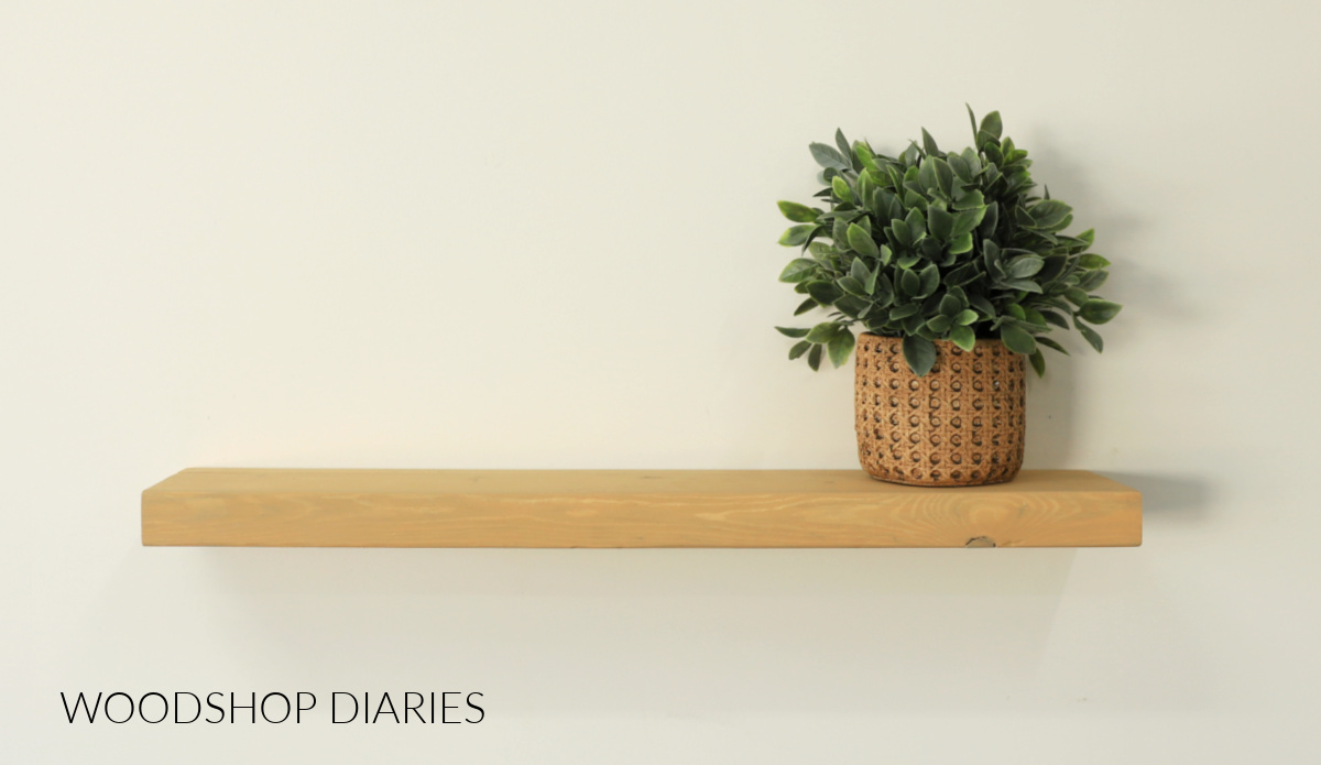 Finished DIY wooden wall shelf made using dowels hanging on wall with faux plant
