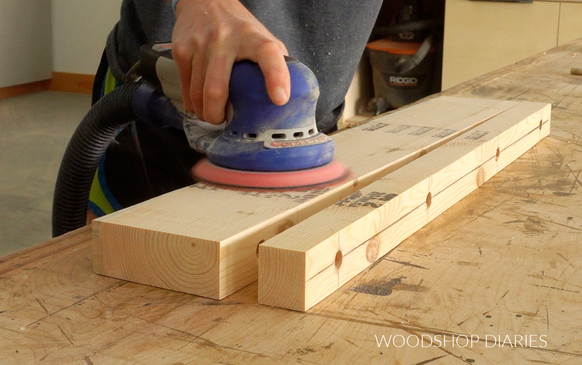 Close up of Shara Woodshop Diaries sanding 2x6 board for floating shelf