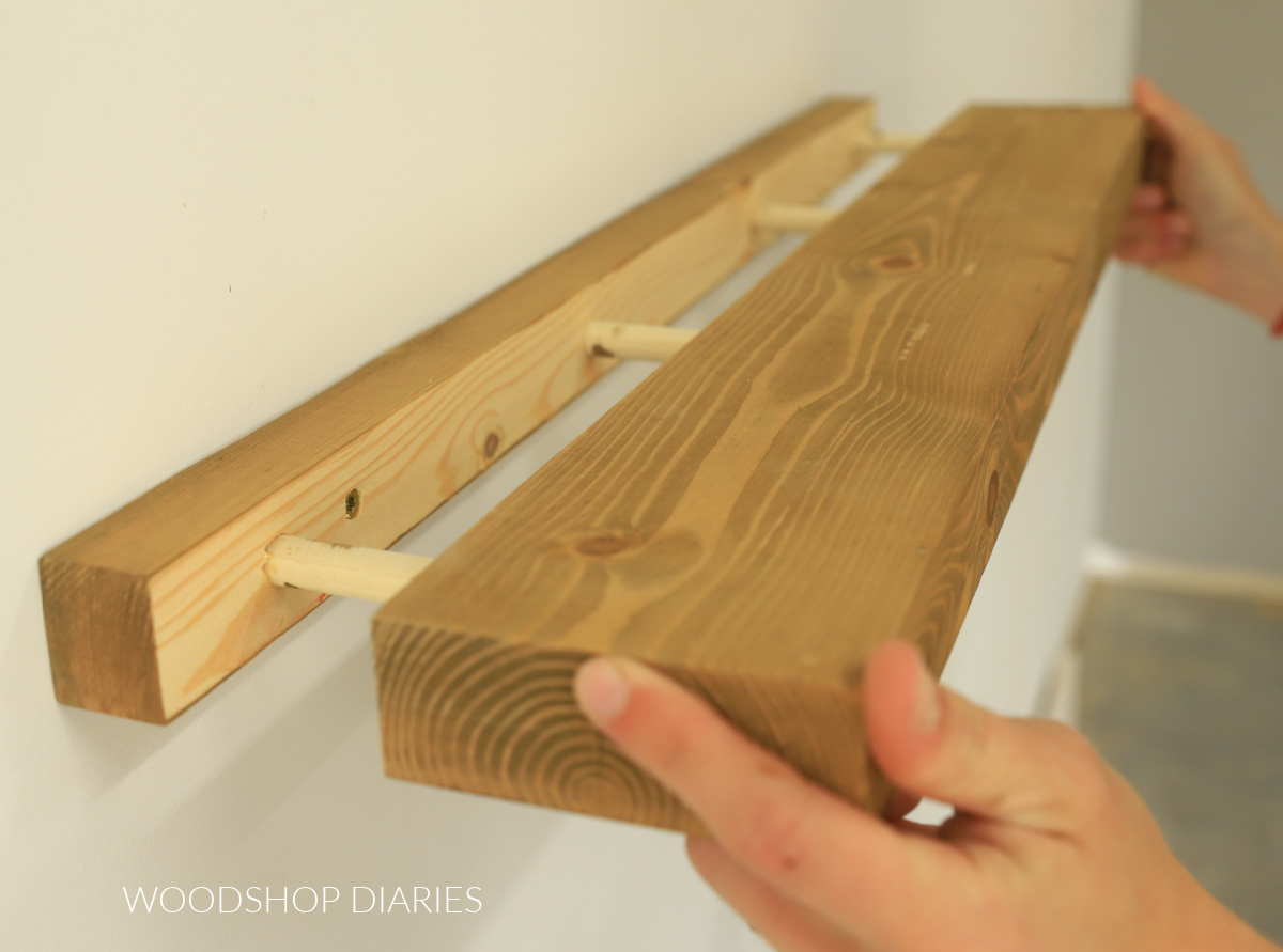 Close up sliding floating shelf board into dowel rods to hang