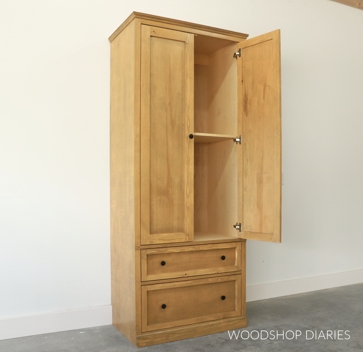 Finished DIY armoire cabinet with drawers. Top section with double doors and one door open to reveal shelving inside